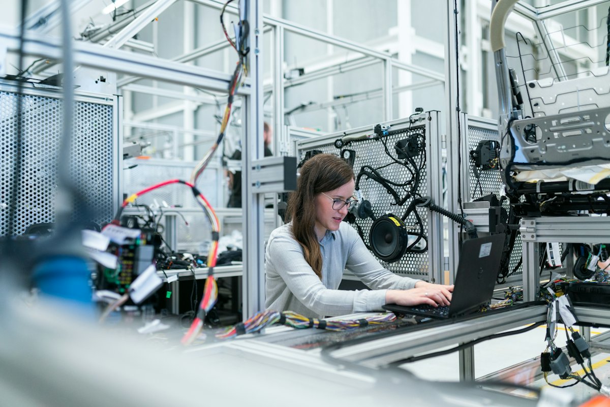 An engineer at a laptop beside a wiring harness on a lab bench.